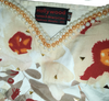 Close-up of a decorative fabric with floral patterns and pearl embellishments, featuring the 'Hollywood Fashion & Beauty Corp.' label.