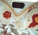 Close-up of a decorative fabric with floral patterns and pearl embellishments, featuring the 'Hollywood Fashion & Beauty Corp.' label.